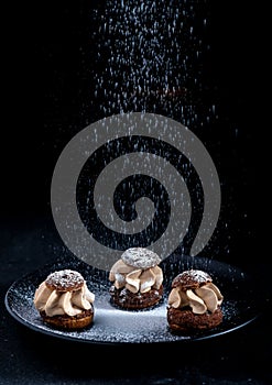 Shu cake sprinkled with powdered sugar on a black background