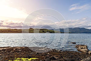 Shuna Island basks in warm sunlight, viewed from the tranquil rocky shores of Oban, Loch Linnhe