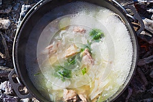 Shurpa soup in a large cast-iron cauldron outdoor. Summer food for hike. Top view.