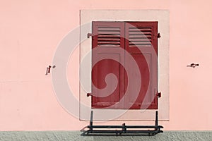 Shutter window with closed wooden boards on a pink wall