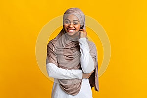 Shy black muslim girl in headscarf posing over yellow background