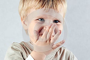 Shy blond boy hide his nose and mouth with hid hand