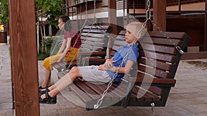 A shy boy and a girl are sitting on a swing bench in a modern courtyard.
