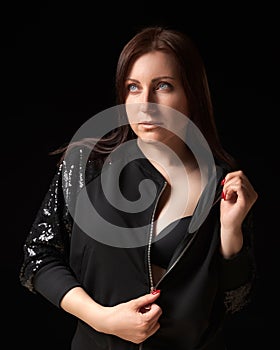 Shy brunette woman unzipping black jacket and showing bra, looking up away. Waist up portrait