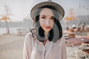 Shy caucasian woman in formal shirt posing on blur nature background. Outdoor photo of interested brunette lady in hat