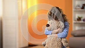 Shy curly girl hiding face behind favorite teddy bear, childhood psychology