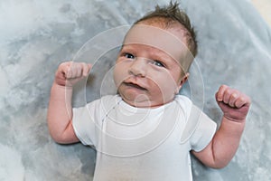 Shy facial expression. Adorable caucasian newborn baby boy in white t-shirt looking bashfully at camera and clenching