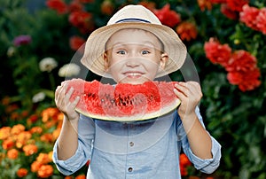 Shy little boy in a he holds a large slice of watermelon and hides his face outdoors. A cute boy in a straw hat is