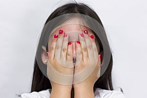 Shy little girl covers her face with hands showing pink polish nails