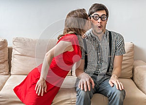 Shy man is surprised by kiss from woman sitting on sofa. Dating concept