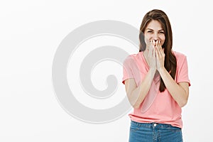 Shy and timid cute european female in pink t-shirt and jeans, chuckling and covering mouth with palm, laughing quietly