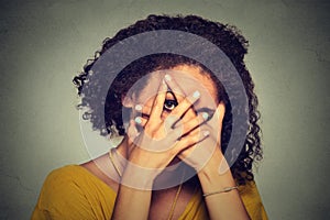 Shy woman hiding face timid. Woman peeking though hands. Gray background.