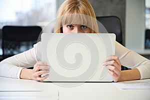 Shy woman hiding her face behind laptop