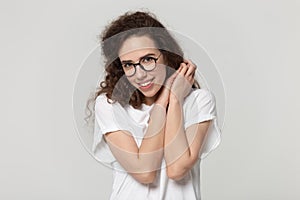 Shy young attractive girl in eyeglasses holding hand near shoulder.