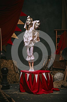 Siamese twin girls in white vintage costumes with makeup standing over dark retro circus backstage background. Creative