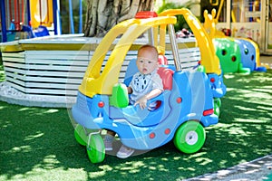 Sian 1 year old toddler baby boy child riding on a colorful small toy car at play ground in the day time