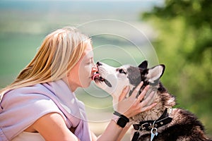 Siberian husky licks in the face of his mistress, who hugs him against the backdrop of a forest road on a sunny day