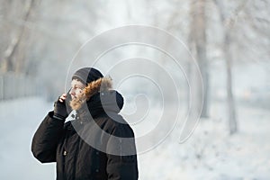 Siberian man talking on the phone outdoors by cold day in a warm winter down jacket with fur hood. Snow frost