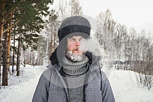 Siberian Russian man with a beard in hoarfrost in freezing cold in the winter freezes and wears a hat with a earflap