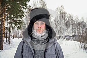 Siberian Russian man with a beard in hoarfrost in freezing cold in the winter freezes and wears a hat with a earflap