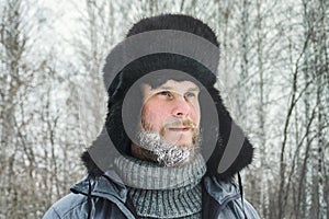 Siberian Russian man with a beard in hoarfrost in freezing cold in the winter freezes and wears a hat with a earflap