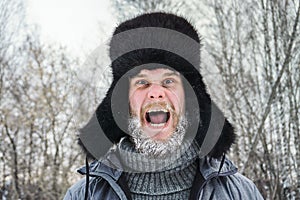 Siberian Russian man with a beard in hoarfrost in freezing cold in the winter freezes and wears a hat with a earflap