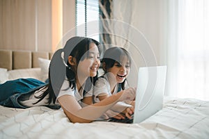 Sibling Asian girl child on the bed and learning online on a laptop Internet. Virtual class lesson on video during self isolation