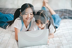 Sibling Asian girl child on the bed and learning online on a laptop Internet. Virtual class lesson on video during self isolation