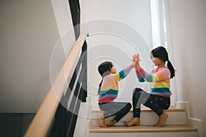 Sibling Asian girls playing rock paper scissors hand game. children sitting on stairs at home playing together