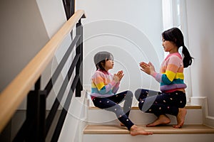 Sibling Asian girls playing rock paper scissors hand game. children sitting on stairs at home playing together