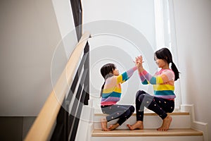 Sibling Asian girls playing rock paper scissors hand game. children sitting on stairs at home playing together