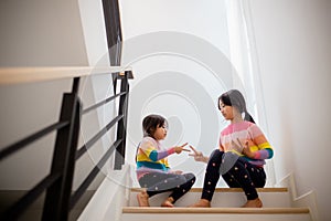 Sibling Asian girls playing rock paper scissors hand game. children sitting on stairs at home playing together