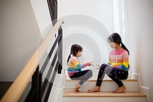 Sibling Asian girls playing rock paper scissors hand game. children sitting on stairs at home playing together