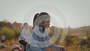 Sibling asian girls riding a bicycle and enjoying with nature together with sunrise in the morning time.