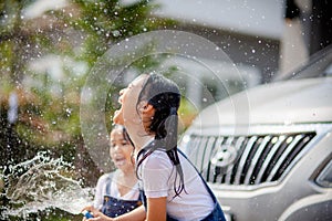 Sibling Asian girls wash their cars and have fun playing indoors on a hot summer day