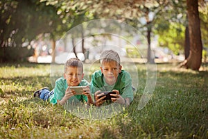 Sibling boy playing game on mobile together lying on grass in park sunny day.