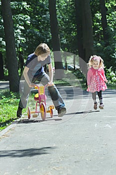 Sibling children happy playing tag game by running and riding kids tricycle