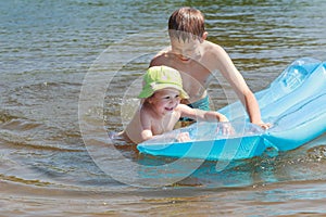 Sibling children having fun with inflatable blue pool lilo in summer lake outdoor