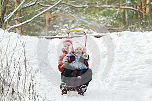 Sibling children having fun sliding down snowy hill during winter time