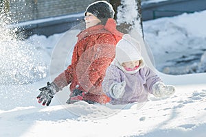 Sibling children making snowstorm by tossing up snow during frosty winter sunny day outdoors