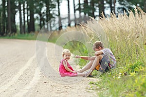 Sibling children playing in dust sitting on summer dirt road