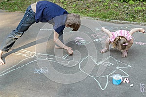 Sibling children playing during sidewalk chalking on asphalt surface