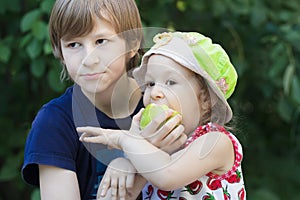 Sibling children sharing green apple fruit outdoor