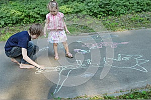 Sibling children sharing sidewalk chalks and drawing on asphalt surface