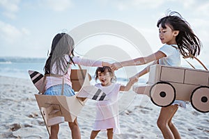 sibling and girl friend playing with cardboard airplane and car on the beach