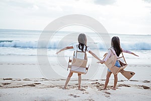 sibling and girl friend playing with cardboard airplane and car on the beach