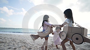 sibling and girl friend playing with cardboard airplane and car on the beach