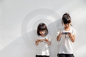 Sibling girls watching their smartphones on white background. Social concept about new technology people addiction