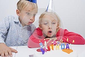 Siblings blowing birthday candles at table