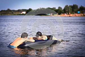 Siblings brother and sister with inflatable matrass swim in the lake on sand beach background